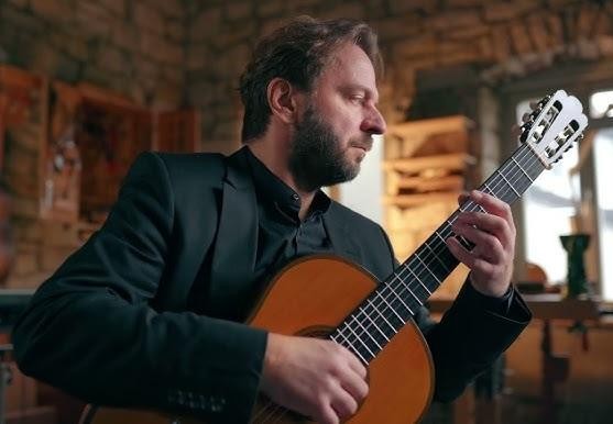 Marcin Dylla w trakcie emocjonującego występu na scenie, grający na gitarze klasycznej.